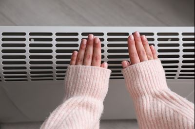 Gros plan d'une femme se réchauffant les mains près d'un radiateur électrique.
